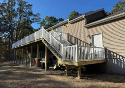A wooden deck with white railings and stairs leads to a home nestled among trees, showcasing outdoor living space.